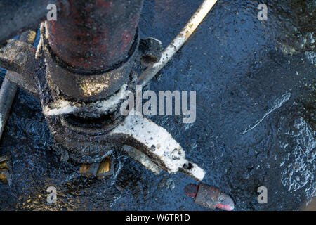 Eine Nahaufnahme von der Oberfläche des schwarzen Verschmutzung durch Öl auf dem Wasser. Nahaufnahme von einer Ölpest in Wasser mit Herbstfarben im Gras am Ufer. Stockfoto