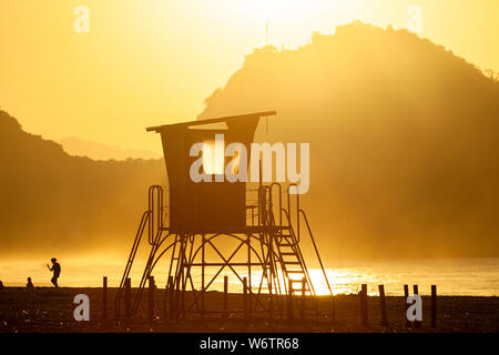 Silhouette eines alten Rettungsschwimmer Turm vor einem leuchtenden Dunst am Strand von Copacabana in Rio de Janeiro mit Hintergrundbeleuchtung durch die intensiven goldenen Stunde Sonnenlicht mit Stockfoto