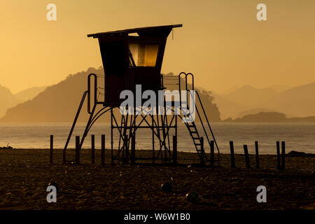 Silhouette eines alten Rettungsschwimmer Turm vor einem leuchtenden Dunst am Strand von Copacabana in Rio de Janeiro mit Hintergrundbeleuchtung durch die intensiven goldenen Stunde Sonnenlicht mit Stockfoto