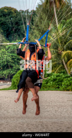 Eine Frau aus Saudi Arabien geht Parasailing am Batu Ferringhi Strand auf Penang, Malaysia Stockfoto