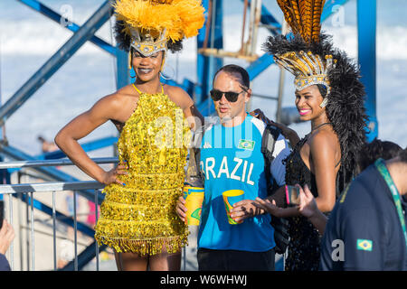 Mann mit zwei Frauen im Karneval Outfit während der Olympischen Spiele 2016 auf einen temporären Stand am Strand von Copacabana mit dem Ozean im Hinterg Stockfoto