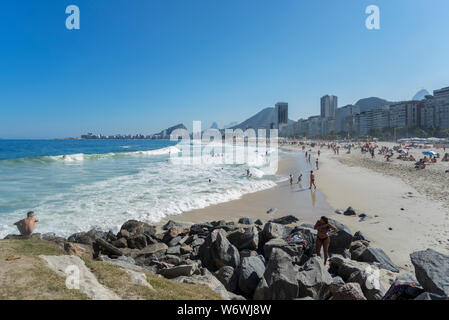 Strand von Copacabana auf einem hellen, sonnigen Tag mit blauen Himmel mit typischen Nachbarschaft Bergkulisse im Hintergrund und Felsen im Vordergrund Stockfoto