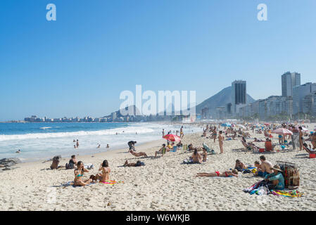 Besucher in Copacabana Strand an einem sonnigen Tag mit blauen Himmel mit typischen Nachbarschaft Bergkulisse im Hintergrund Stockfoto