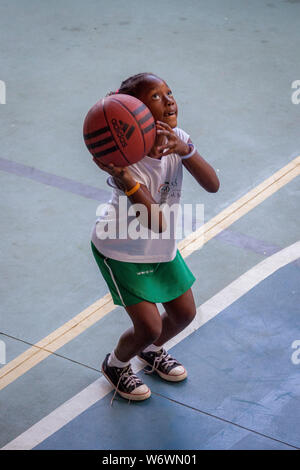 Junges Mädchen mit Basketball in den Händen konzentriert und bereit mit Knie gebeugt, die Kugel zu werfen Stockfoto