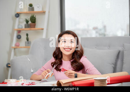 Lächelnde Mädchen schneiden valentine Herz aus rotem Papier mit einer Schere im Wohnzimmer Stockfoto