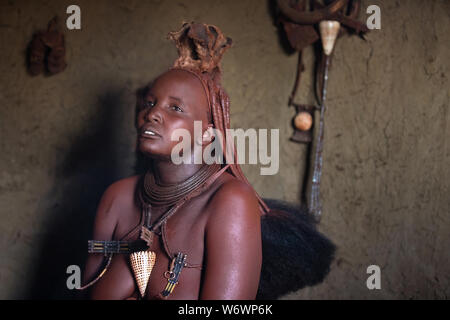 Opuwe, Namibia - Juli 12, 2019: Ein traditionelles Himba Frau nach Durchführung ihrer täglichen Schönheit Verfahren von Kampor baum Rauch- und ockerfarbene Stein pow Stockfoto