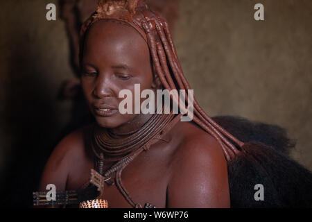 Opuwe, Namibia - Juli 12, 2019: Ein traditionelles Himba Frau Porträt in ihr dunkles Lehmhütte. Stockfoto