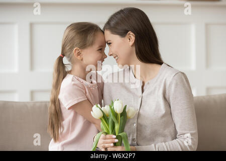 Happy Mother Holding weißen Tulpen berührt Stirn mit Tochter Stockfoto