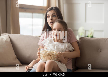 Mutter halten Tochter auf dem Schoß ansehen Film fühlt sich schockiert Stockfoto