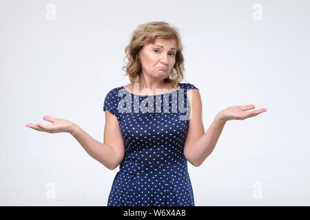 Verwirrte ältere Frau im blauen Kleid zuckt mit den Schultern, als keine Antwort wissen, Stockfoto