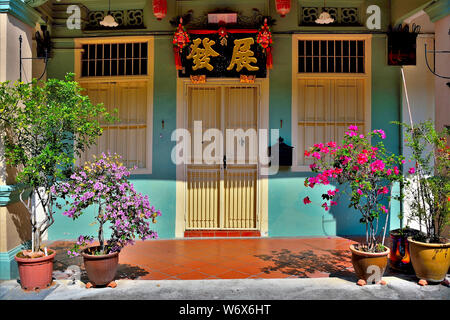 Eingang zu den traditionellen Peranakan shop Haus mit Sahne die Tür und die Fenster auf der blauen Wand mit tropischen Pflanzen im historischen Geylang, Singapur Stockfoto