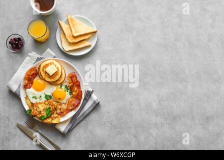 Amerikanisches Frühstück auf grau, Ansicht von oben, kopieren. Sonnenseite gebratene Eier, gebratenen Speck, Hash Brown, Pfannkuchen, Toast, Orangensaft und Kaffee für Stockfoto