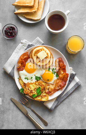 Amerikanisches Frühstück auf grau, Ansicht von oben, kopieren. Sonnenseite gebratene Eier, gebratenen Speck, Hash Brown, Pfannkuchen, Toast, Orangensaft und Kaffee für Stockfoto