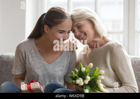 Mutter erwachsene Tochter sitzen auf Stuhl mit Geschenke und Blumen Stockfoto