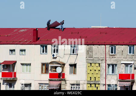 Batumi, Georgien, 2019-03-04: Zwei Männer auf dem Dach eines mehrstöckigen Gebäude machen Reparaturen - Sie Schiefer ändern. Stockfoto