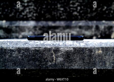 MONOLITH: Ein Handy sitzt im Profil auf einer Steinstufe. Stockfoto