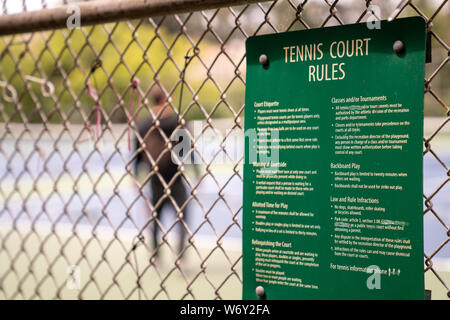 Tennisplatz Regeln veröffentlicht außerhalb einer Gemeinschaft Tennisplatz mit Mann spielt im Hintergrund Stockfoto