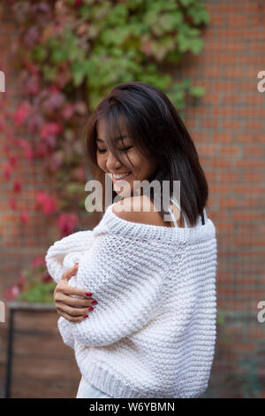 Schöne asiatische Mädchen lächelnd und sie ist in Strickjacke in der Nähe von Mauer und lockig wild bunte Trauben Stockfoto