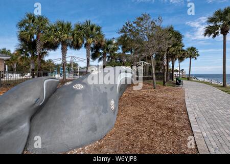 Ein Wal Skulptur in Neptun Park mit der St. Simons Leuchtturm hinter entlang der Saint Simons Sound in St. Simons Island, Georgia. Der Leuchtturm wurde in der ersten im Jahre 1807 gebaut, aber durch die konföderierten Truppen 1862 zerstört, bevor er im Jahr 1872 wieder aufgebaut. Stockfoto