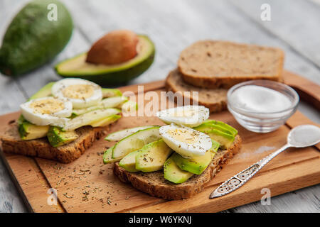 Zwei Scheiben leckere Sandwiches Avocado mit Ei und Gewürze auf einem Holzbrett. Konzept der Keto Diät Stockfoto