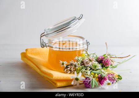 Frische Blumen Honig im Glas und Blumen auf weißem Hintergrund Stockfoto