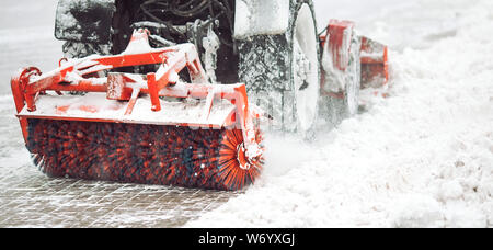 Stadt Service Reinigung Schnee, ein kleiner Traktor mit einer rotierenden Bürste löscht eine Straße in der Stadt park von den frisch gefallenen Schnee im Winter Tag Stockfoto