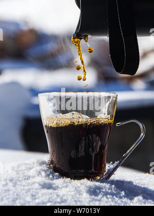 Kaffee ist in ein Glas Schale von einer Thermoskanne auf einem Haufen Schnee gegossen Stockfoto