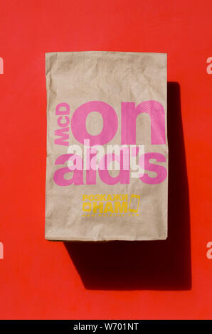 Charkiw, UKRAINE - August 1, 2019: Nahaufnahme von einem McDonald's Take away Food braune Papiertüte auf rotem Hintergrund. McDonald's ist ein Schnellimbiss Restaurant Cha Stockfoto