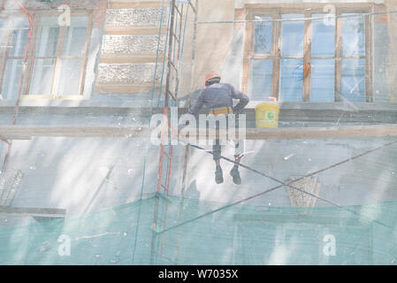 Ein Mann sitzt auf einem Gerüst und stellt das Gebäude. Der Baumeister malt die Wände des Gebäudes und die Fassade in einer Höhe. Stockfoto