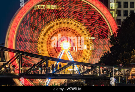 03.August 2019 Hessen, Frankfurt/Main: ein Riesenrad der Mainfest dreht sich hinter dem Eisernen Brücke, eine Brücke über den Fluss (Foto mit langen Exposition). Die traditionelle Folk Festival am Mainufer findet vom 2. August bis zum 5. August 2019. Entsprechend der Stadt, das wichtigste Festival, das erstmals im Jahre 1340 gefeiert wurde zu weihen, in der Nähe der Dreikönigskirche (Kirche der Heiligen Drei Könige), war ursprünglich eine Rettungsleine, die von Fischern und Matrosen zu den Wichtigsten betrachtet. Foto: Frank Rumpenhorst/dpa Stockfoto