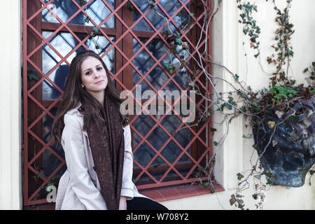 Junge Frau in einem stilvollen beige Graben draussen, lächeln in die Kamera schaut. Im Frühling oder Herbst. Stockfoto