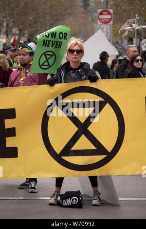 Junge blonde Frau in Schwarz Sonnenbrille und schwarze Lederjacke trotzig Holding Holding ein großes gelbes Klima Not Banner. Stockfoto