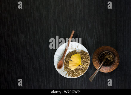 Künstlerische Fotografie der Yerba Mate und Ginkgo Biloba Blätter oder Blatt Infusion, typische aus Argentinien, in eine weiße Platte, über einem dunklen Holz- backgrou Stockfoto