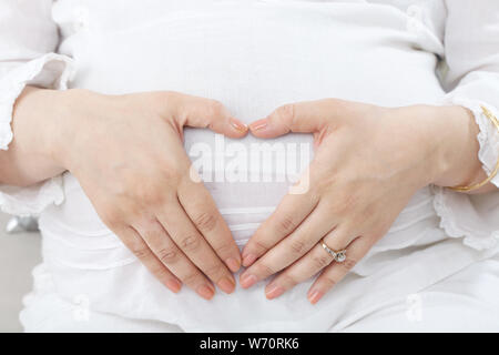 Schwangere Frau mit Bauch mit ihren Fingern bilden eine Herzform Stockfoto