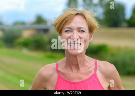 Verspielt blonde Frau, eine käsige toothy Grinsen, als sie sich mit den Händen auf den Hüften draußen im Land Stockfoto