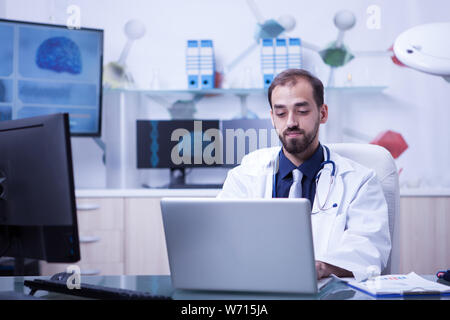 Schwere Arzt Eingeben einer Behandlung auf seinem Laptop. Arzt in einem Labor arbeiten. Stockfoto