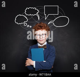 Niedliche Kind Junge in Anzug und Brille mit leeren Rede wolken Blasen auf blackboard Hintergrund Stockfoto