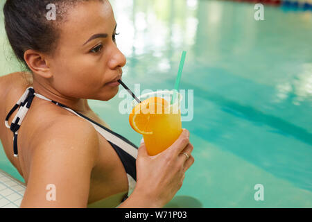 Porträt der jungen gemischten Rasse Frau trinkt Cocktail im Pool und genießen Sie einen luxuriösen Wellnessbereich, kopieren Raum Stockfoto