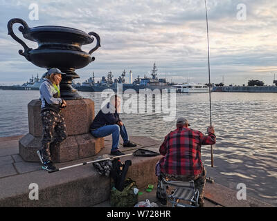 SAINT-Petersburg, Russland - Juli 23, 2019: Fischer fangen in Kronstadt, auf dem Hintergrund der Kriegsschiffe. Stockfoto
