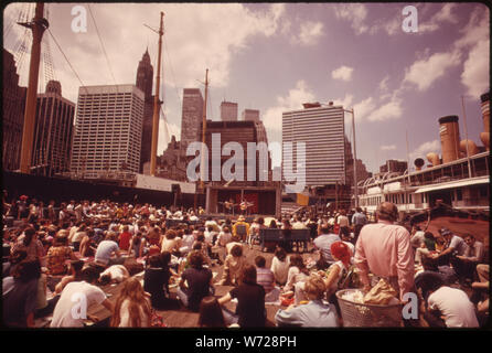 FOLK Singen und Tanzen HAT EIN NEUES ZUHAUSE GEFUNDEN AM South Street Seaport auf dem East River in der Nähe der Brooklyn Bridge. Begeisterte Zuschauer versammeln sich mehrmals in der Woche während des Sommers ZU GENIESSEN DIE SHOW UND DIE MUSIK, Blick auf den Hafen, Boote, und atmen Sie die Luft Stockfoto