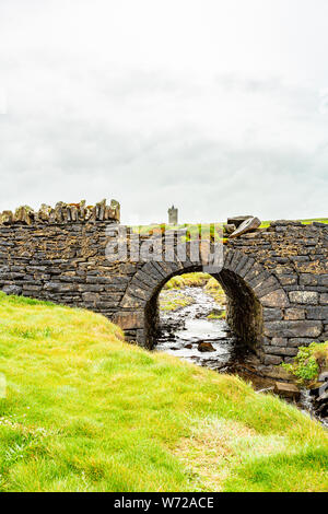 Alte steinerne Brücke an der Küste zu Fuß Route mit dem Schloss Doonagore im Hintergrund von Doolin zu den Klippen von Moher, die wilden Atlantik Weg Stockfoto