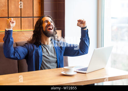 Portrait von Happy screaming hübscher junger erwachsener Mann Freiberufler in lässigen Stil im Cafe und mit Laptop sitzen, feiern das Ziel der fooftball überein Stockfoto