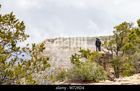 Grand Canyon, Arizona, USA. 22. Mai 2019. Zwei Männer in schwarzen Anzügen und Hüte mit Blick auf die roten Felsen Schlucht, bewölkter Himmel Stockfoto