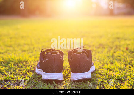 Close up neue Paare schwarz Schuhe/Sneaker Schuhe auf der grünen Wiese im Park bei Sonnenuntergang. Worm Ton, Sonnenlicht und lens flare Effekt w Stockfoto