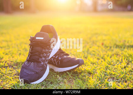 Close up neue Paare schwarz Schuhe/Sneaker Schuhe auf der grünen Wiese im Park bei Sonnenuntergang. Worm Ton, Sonnenlicht und lens flare Effekt w Stockfoto