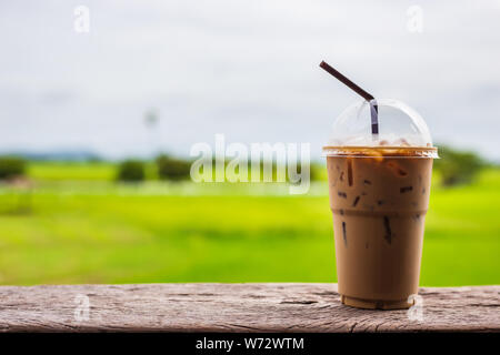 Close up Eiskaffee in Schale aus Kunststoff mit Trinkhalm auf der Terrasse und grünes Feld Hintergrund Stockfoto