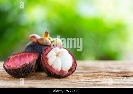 Lila Mangostanfrucht auf hölzernen Tisch mit grünem Hintergrund Weichzeichner light Space Hintergrund für Text, Design, Fotomontage oder Werbung Stockfoto