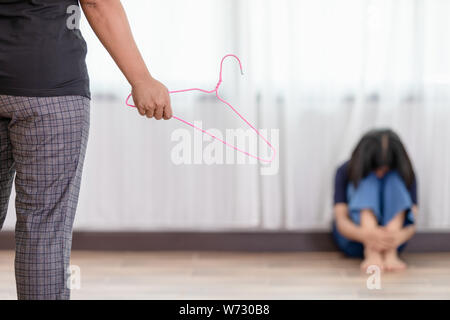 Die Mutter ihre Tochter zu bestrafen. Frau mit Kleiderbügel und ihre Tochter sitzen auf dem Boden. Bestrafung Konzept Stockfoto