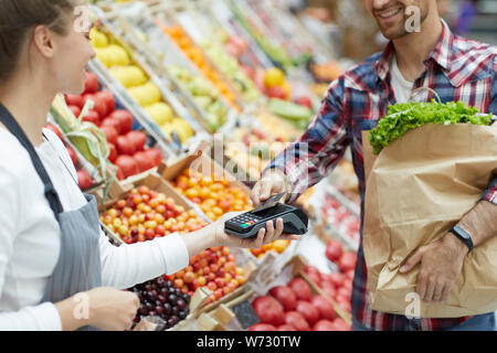 Den mittleren Abschnitt Portrait von gutaussehenden jungen Mann bezahlen per Smartphone bei Farmers Market, Kopie Raum Stockfoto