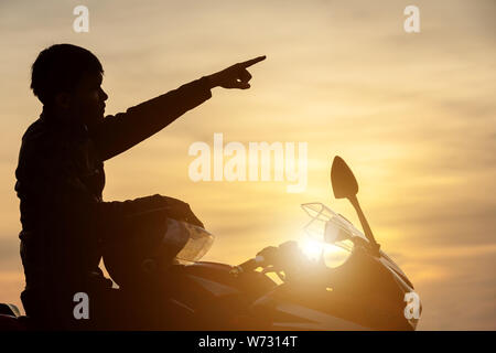 Stattliche Motorradfahrer Punkt der Finger in den Himmel. Silhouette des Motorradfahrers im Sonnenuntergang Stockfoto